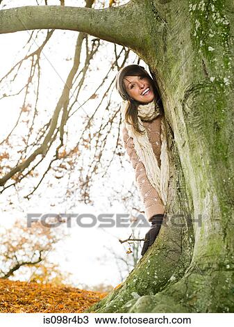 Stock Image - Smiling woman standing behind a tree. Fotosearch