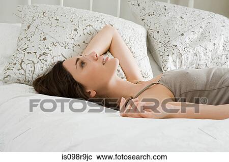 Young woman lying on bed View Large Photo Image Stock Image - Young woman lying on bed. Fotosearch