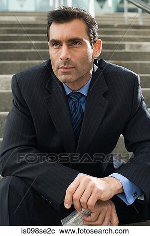 Stock Image - A businessman sitting on steps holding a newspaper. Fotosearch
