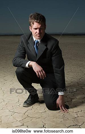 Stock Photo - Businessman crouching in desert landscape. Fotosearch