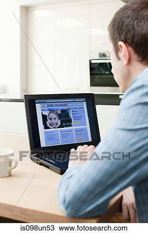 Stock Image - Young man looking at insurance on laptop. Fotosearch