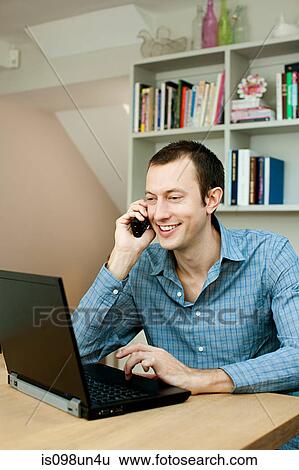 Stock Photograph - Young man using laptop and phone. Fotosearch