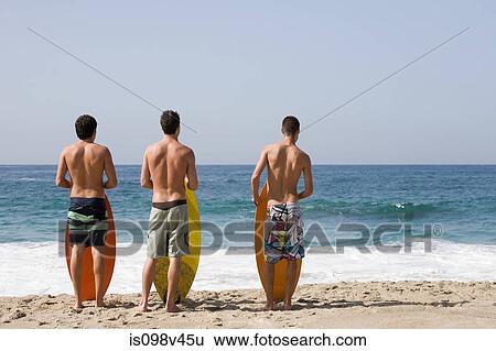 Stock Photograph - Three young men on beach with surfboards. Fotosearch