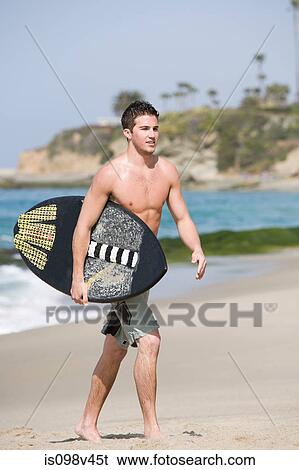 Young man carrying surfboard on beach View Large Photo Image Stock Photograph - Young man carrying surfboard on beach. Fotosearch