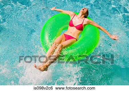 Stock Photograph - Young woman floating on green inflatable ring in swimming pool. Fotosearch