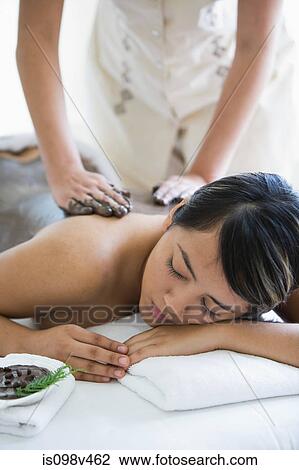 Stock Image - Young woman having mud mask applied to back. Fotosearch