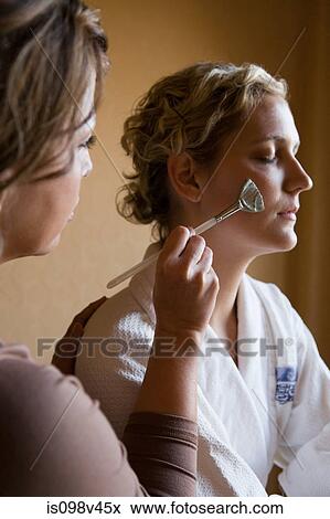 Stock Photo - Young woman having mud mask applied to face. Fotosearch