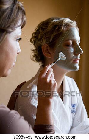 Stock Photo - Young woman having mud mask applied to face. Fotosearch