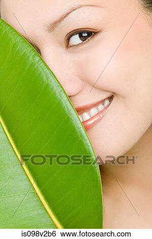 Stock Photograph - Young woman hiding behind green leaf. Fotosearch