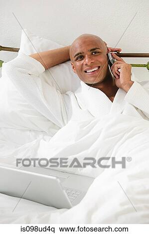Man in bed with laptop and cellphone View Large Photo Image Stock Photography - Man in bed with laptop and cellphone. Fotosearch