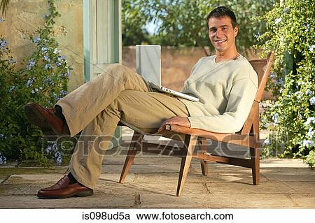 Stock Image - Man sitting in a lounge chair with laptop. Fotosearch