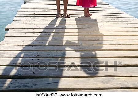 Stock Photo - Shadows of child and adult on jetty. Fotosearch