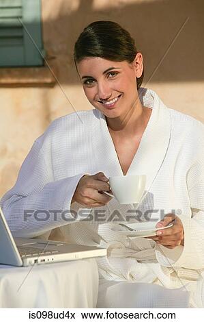 Stock Photo - Woman in bathrobe with coffee and laptop. Fotosearch
