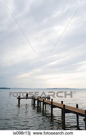 Stock Image - Woman sitting on a jetty. Fotosearch