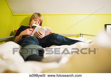 Stock Image - Boy reading book on bed. Fotosearch