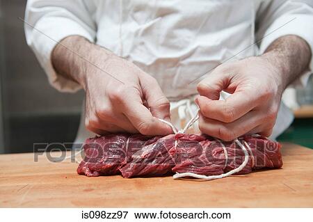 Stock Photo - Butcher tying beef tenderloin with string. Fotosearch