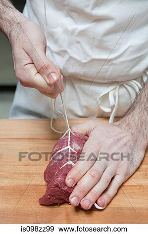 Stock Photo - Butcher tying beef tenderloin with string. Fotosearch