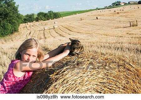 Stock Image - Girl with cat on hay bale in field. Fotosearch