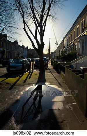 Stock Image - Puddle on pavement with houses. Fotosearch