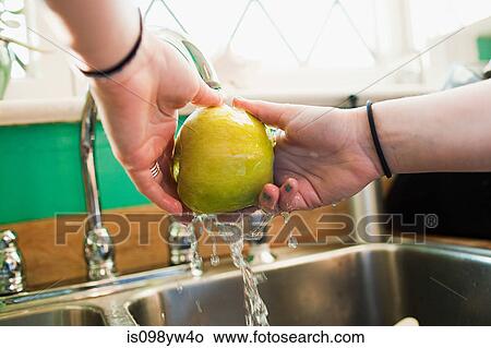 Picture - Teenage girl washing apple in kitchen sink. Fotosearch