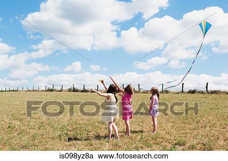 Stock Image - Three girls flying kite in field. Fotosearch
