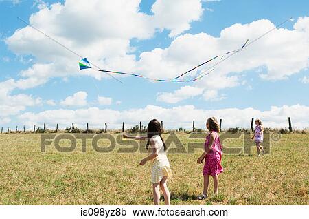 Three girls flying kite in field View Large Photo Image Stock Image - Three girls flying kite in field. Fotosearch