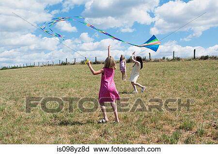 Stock Image - Three girls flying kite in field. Fotosearch