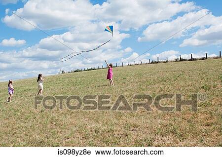 Stock Image - Three girls flying kite in field. Fotosearch