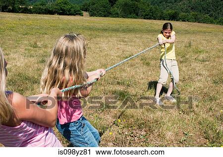 Three girls playing tug of war in field View Large Photo Image Stock Image - Three girls playing tug of war in field. Fotosearch