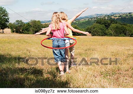 Stock Photo - Three girls walking in field with plastic hoops. Fotosearch