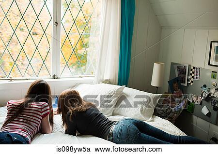 Stock Image - Two teenage girls lying on bed. Fotosearch