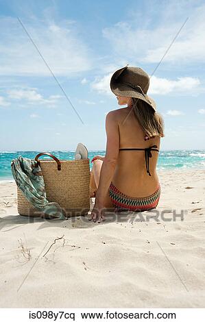 Stock Photography - Woman sitting on sandy beach, Mustique, Grenadine Islands. Fotosearch