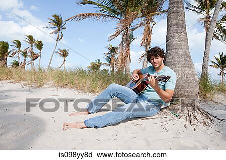 Stock Image - Young man playing guitar on beach, portrait. Fotosearch
