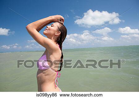 Stock Photograph - Young woman in sea with arms up, portrait. Fotosearch