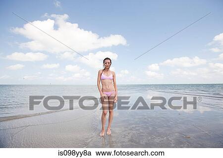 Stock Image - Young woman standing in shallow sea, portrait. Fotosearch