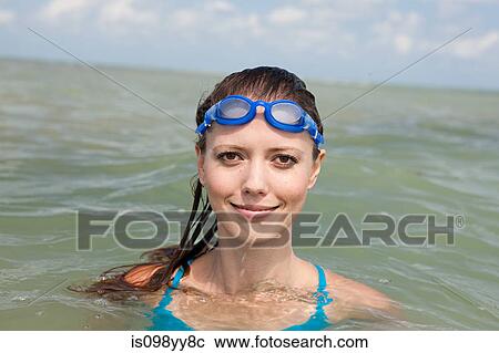 Stock Image - Young woman wearing swimming goggles in sea, portrait. Fotosearch