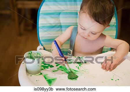 Stock Image - Baby boy sitting in high chair painting picture. Fotosearch
