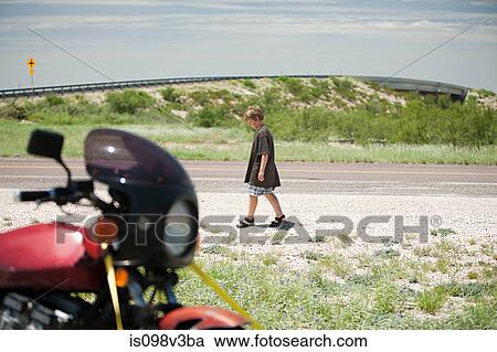 Stock Image - Boy walking past motorbike. Fotosearch