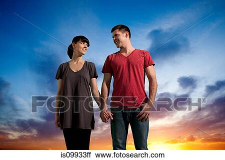 Couple holding hands against dramatic sunset View Large Photo Image Stock Image - Couple holding hands against dramatic sunset. Fotosearch
