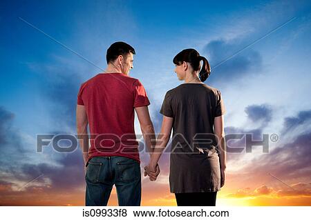 Couple holding hands against dramatic sunset, rear view View Large Photo Image Stock Photo - Couple holding hands against dramatic sunset, rear view. Fotosearch