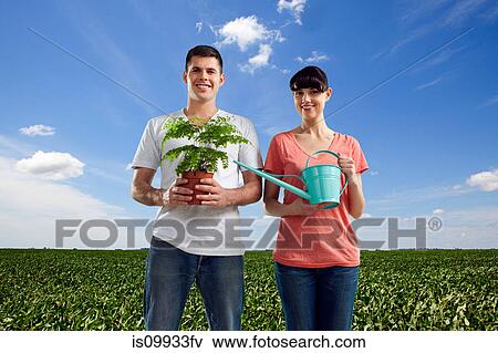 Stock Photo - Couple in field holding plant and watering can. Fotosearch