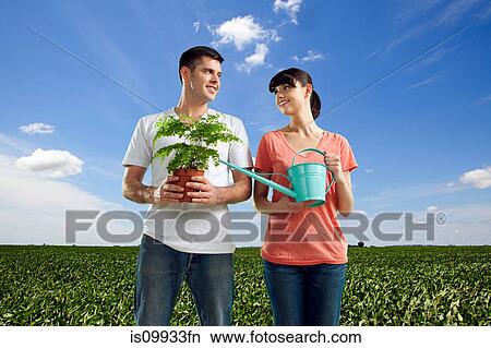 Couple in field with watering can and plant View Large Photo Image Picture - Couple in field with watering can and plant. Fotosearch