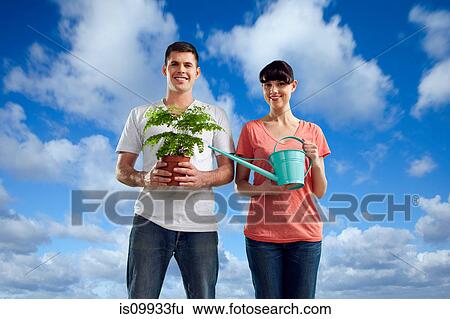 Couple in field with watering can and plant View Large Photo Image Stock Photograph - Couple in field with watering can and plant. Fotosearch