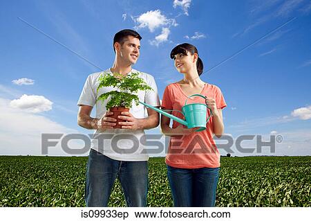 Couple in field with watering can and plant View Large Photo Image Stock Photography - Couple in field with watering can and plant. Fotosearch