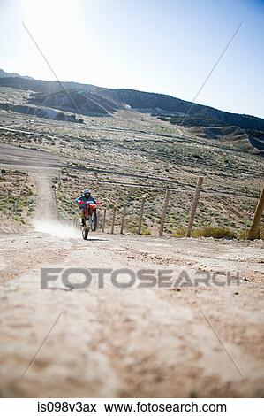 Stock Photo - Man doing wheelie on dirt bike on dirt track. Fotosearch