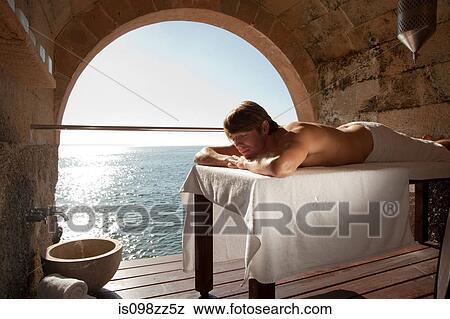 Stock Photo - Man lying on massage table by the ocean. Fotosearch