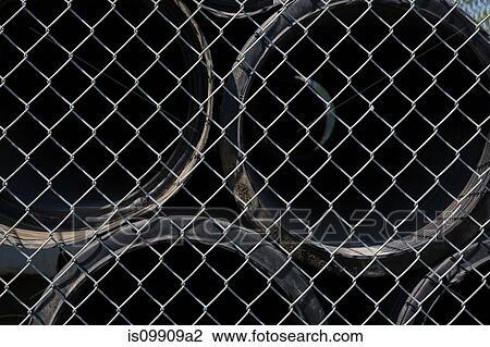 Stock Image - Pipes behind wire mesh fence. Fotosearch
