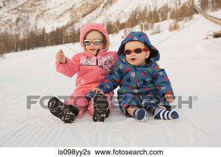 Stock Photograph - Portrait of brother and sister sitting in snow. Fotosearch