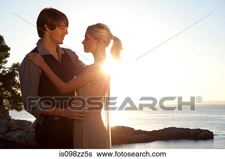 Stock Photograph - Romantic couple by the ocean at sunset. Fotosearch