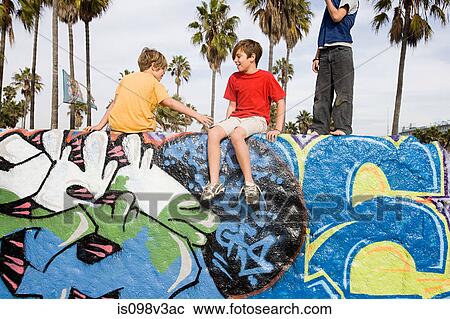 Stock Image - Three boys sitting on wall with graffiti. Fotosearch